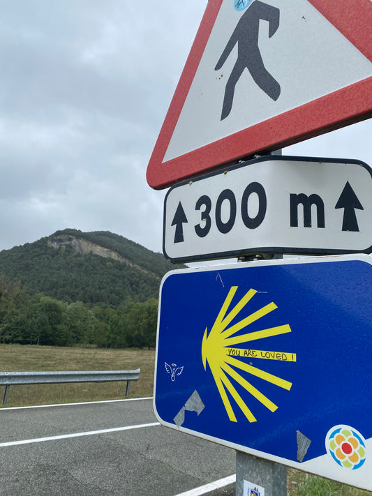 A beautiful view on the Camino de Santiago of a hill and a scallop shell trail marker that says "You are Loved"